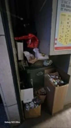 Bac de tri débordant, déchets et cartons déposés hors du bac dans le local poubelles