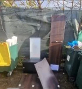 Encombrants (meubles, panneaux de bois) abandonnés au sol à côté des bacs de la résidence